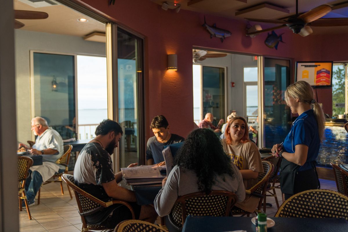 Guests dining at dusk with bay views through the glass